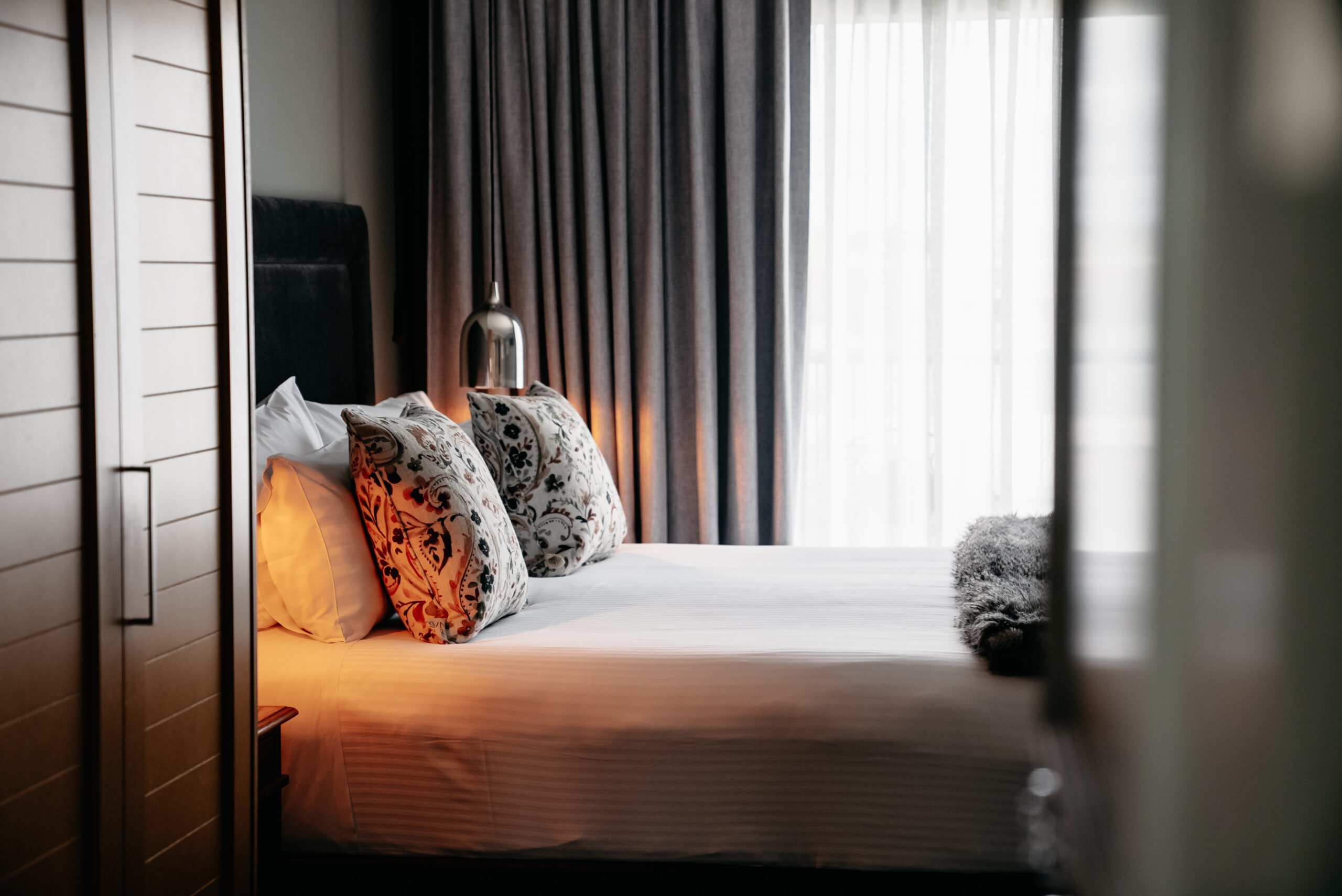 De Russie Boutique Hotel Luxury Room Elegant guest room at De Russie Boutique Hotel Orange featuring a plush bed with decorative cushions, soft ambient lighting, floor-to-ceiling curtains, and a warm, boutique hotel atmosphere designed for a relaxing stay in Orange NSW.